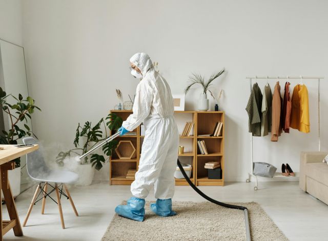 A worker in protective gear disinfecting a modern living room with a fogger.