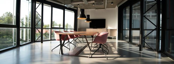 Spacious, sunlit office lounge featuring white tables and chairs with a modern aesthetic.
